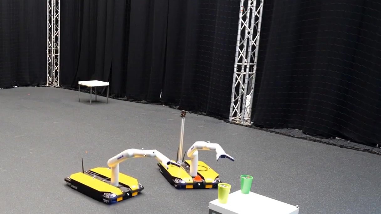 Two mobile manipulators reaching towards a table with cups in the arena (photo 3 of 7)